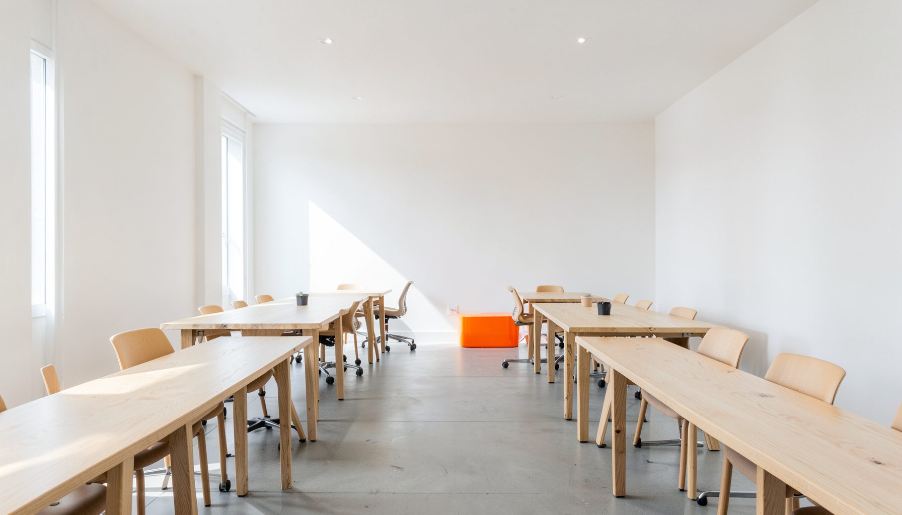 Salle de travail collaborative baignée de lumière naturelle, murs blancs, grandes tables en bois clair, ambiance studieuse