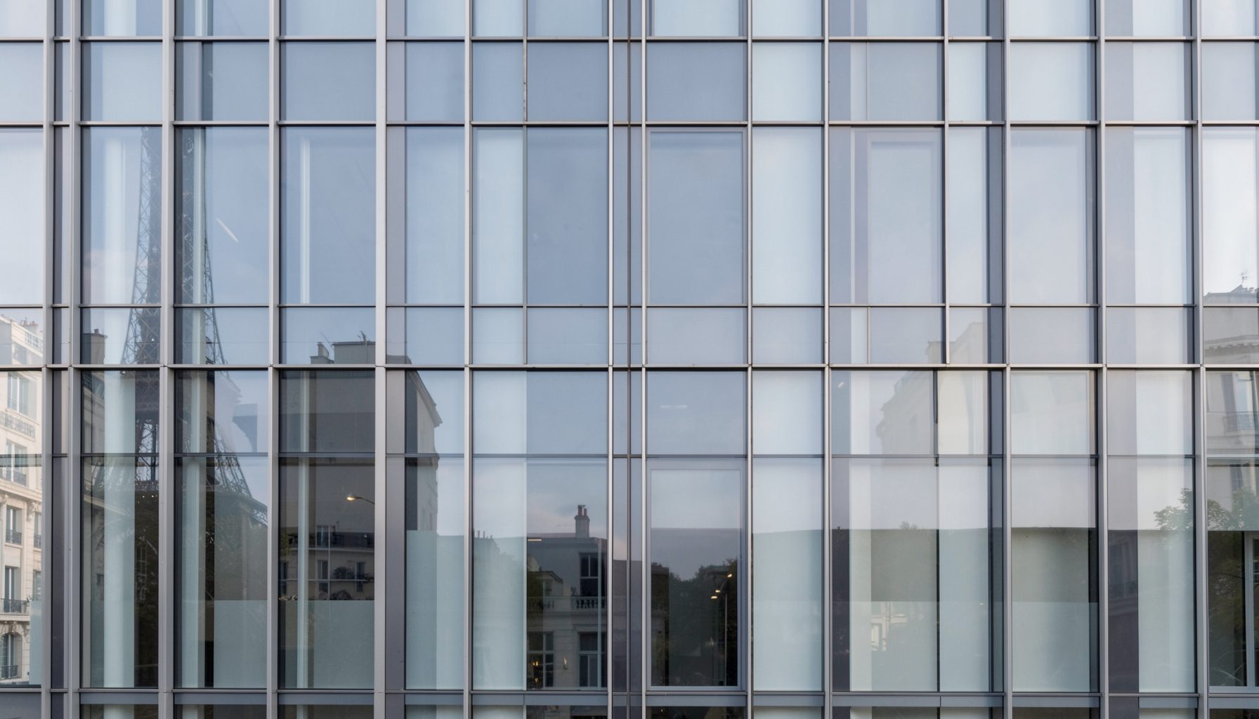 Façade moderne en verre et acier d'un bâtiment parisien, lignes épurées et symétriques sous une lumière naturelle douce